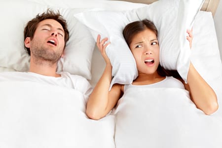 Woman covering her ears with a pillow annoyed with her husband snoring.